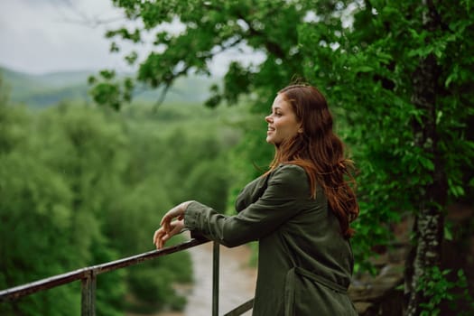 red-haired woman walking in the park looks at the stormy mountain river. Travel, rainy weather