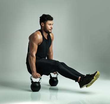 Working every part of his body. Studio shot of a young man working out with kettle bells against a gray background.