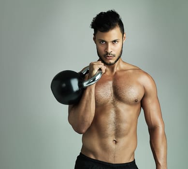 You can see he never skips a gym session. Studio shot of a young man working out with a kettle bell against a gray background.
