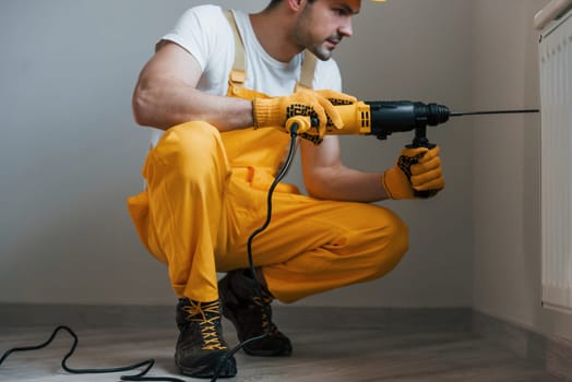 Handyman in yellow uniform works with drill indoors. House renovation conception