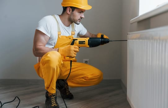 Handyman in yellow uniform works with drill indoors. House renovation conception