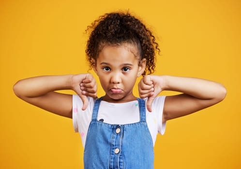 Sad, negative and portrait of a child with a thumbs down isolated on a studio background. Unhappy, fail and a girl kid with an emoji hand sign for frustration, disappointment and disagreement