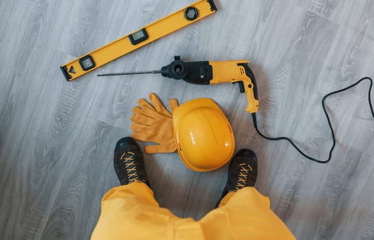 Handyman in yellow uniform with drill standing indoors. House renovation conception