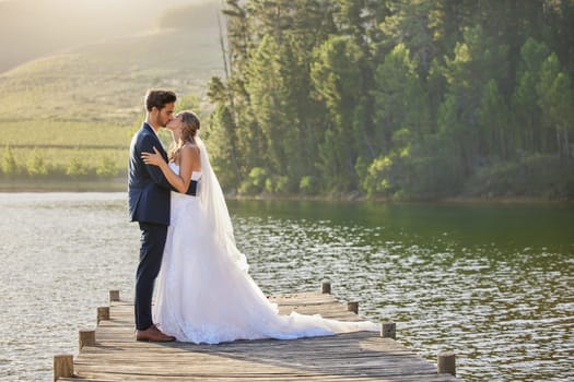 Wedding couple, kissing and hug by lake for love affection, intimate or romantic honeymoon getaway in nature. Man and woman kiss in happiness for marriage relationship or loving embrace outdoors