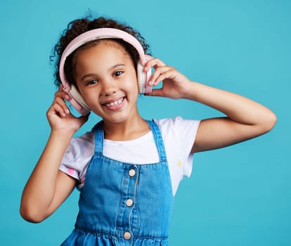 Music, portrait and girl child with headphones in studio for streaming, subscription and audio on blue background. Face, autism and autistic kid happy with noise canceling headphone while isolated