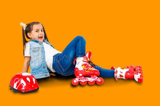 An adorable preschooler smiling though fallen while learning to roller skate. On a orange background.