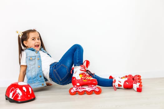 An adorable preschooler smiling though fallen while learning to roller skate. On a white background.