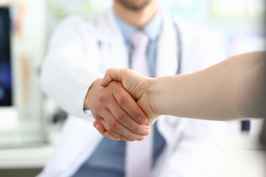 Doctor shaking hands with patient in clinic and thanking handshake for excellent treatment