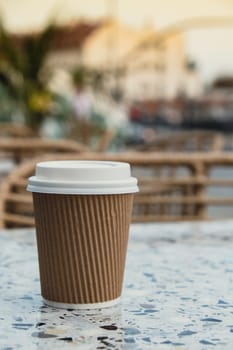 Eco recycling paper cup with coffee or tea on craft paper on table in beach cafe. Take away coffee to go. Copy space for text. Disposable