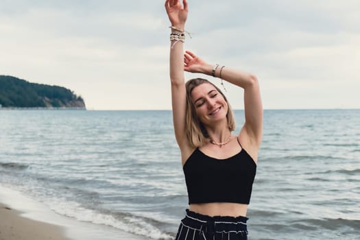 Young woman standing on blurred beachside background. Attractive female enjoying walking the sea shore. travel and active lifestyle concept. Springtime. Relaxation, youth, love, lifestyle solitude with nature. Wellness wellbeing mental health inner peace Slow life