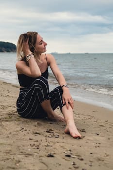 Young woman siting on blurred beachside background. Attractive female enjoying the sea shore. travel and active lifestyle concept. Springtime. Relaxation, youth, love, lifestyle solitude with nature. Wellness wellbeing mental health inner peace Slow life