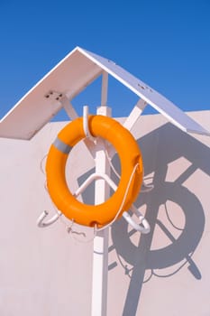 Orange lifebuoy on beach by sea. Safety equipment for rescuing people on seashore. Orange lifebuoy on the pier of blue sky and azure sea
