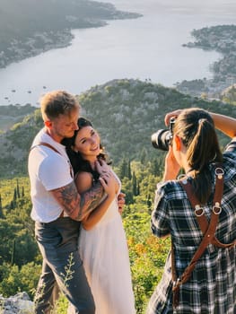 Photographer girl photographs hugging bride and groom on a high mountain