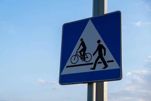 Cyclist and pedestrian route sharing sign. Road sign Pedestrian and bicycle can cross the street here on the background of blue sky