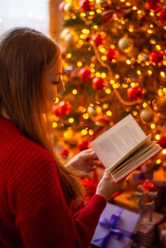 Portrait of a young girl reading a book with bright christmas tree in the background