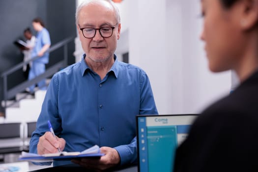 Elderly patient standing at hospital reception signing medical insurance paper