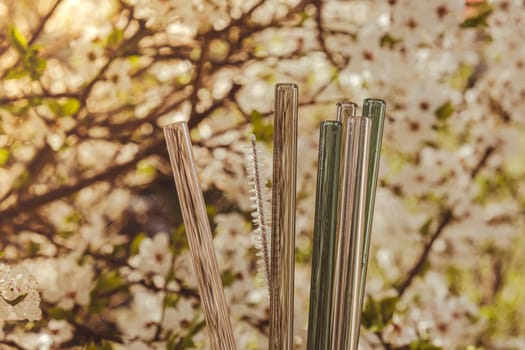 Reusable glass Straws on nature background with green leafs spring flowers Eco-Friendly. Zero waste, plastic free concept. Sustainable lifestyle. Picnic concept