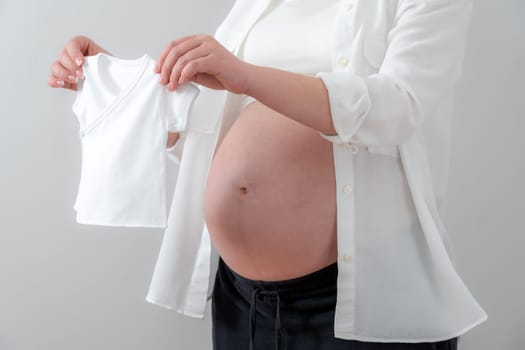 Pregnant woman holding tiny little baby clothes, concept of expecting baby