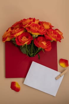 Beautiful red roses flowers in postal red envelope on neutral beige background, empty paper note copy space for text, spring time, greeting card for holiday. Flower delivery. Delicate red yellow roses. Minimal trendy composition. Romantic pastel flowers