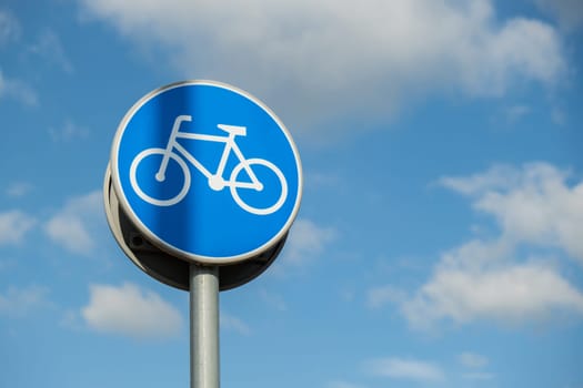 Round road sign depicting white bicycle on blue background, meaning mandatory bike path for cyclists against blue sky background. Blue round sign on bike path pole