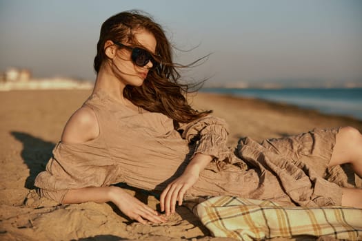 sophisticated red-haired woman in sunglasses lies on the sea coast in windy weather. High quality photo