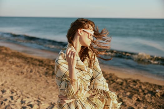 a woman wrapped in a plaid walking along the sea coast straightens her sunglasses