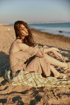 a woman near the sea sits on a blanket and looks into the distance in windy weather. High quality photo