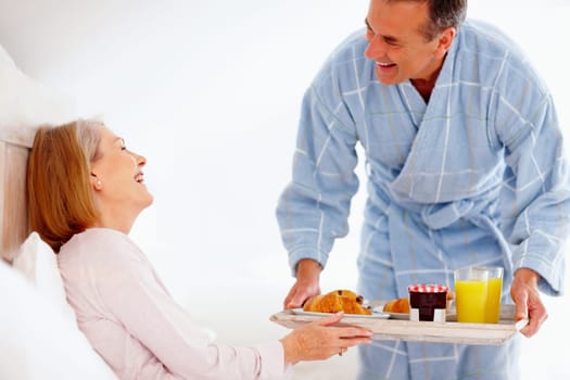 Cheerful mature woman in bed with her husband serving breakfast. Portrait of a cheerful mature woman in bed with her husband serving breakfast.