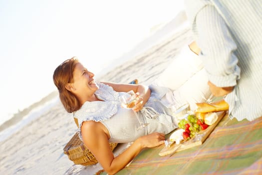 Wine and a romantic picnic. A happy mature woman relaxing on a picnic blanket and enjoying the sunset with her husband.