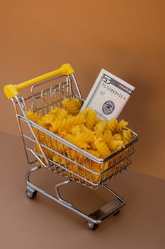 Shopping trolley cart Filled With Pasta with 5 US dollar paper money banknote on Beige background. Copy space for your text. Food and groceries shopping price increase, Rising food cost food crisis inflation concept. Online shopping, buy mall