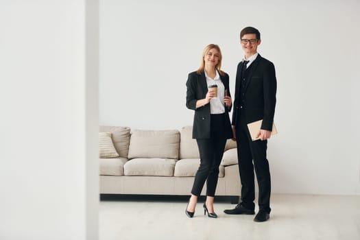 Young guys standing with woman indoors near sofa agaist white wall