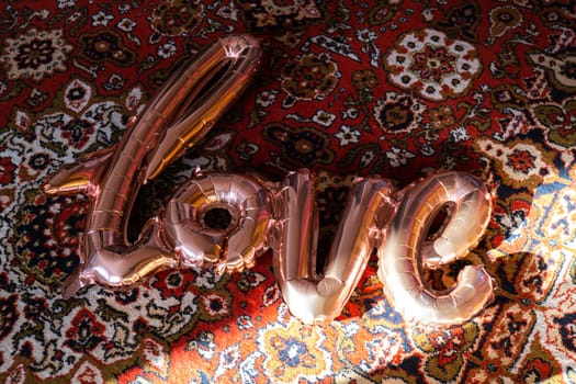 Love text pink foil balloon on authentic Love word from pink inflatable balloon laying carpet. Happy Valentines Day, Mother's Day, birthday concept. Minimalistic creative