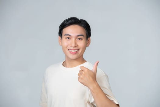 Nice smile friendly Asian man in white t-shirt giving thumbs up