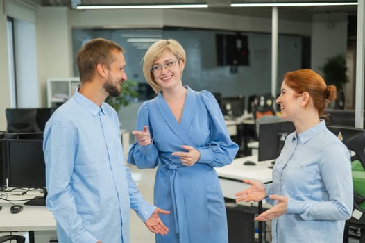 Colleagues communicate at work. Red-haired woman, blonde and bearded man in a denim shirt in the office.