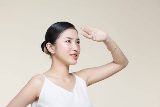 Young asian woman covers her face from the sun with palm against a beige background 