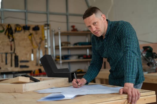 Portrait of a carpenter in a plaid shirt draws a workshop blueprint.