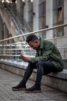 young african american man in jacket messaging online, checking social networks outdoor