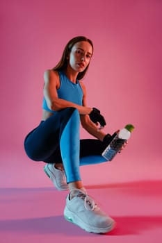 Healthy woman sitting with water bottle in sport clothing over studio background. High quality photo