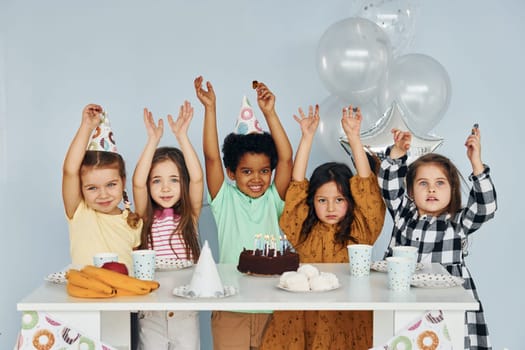 Sits by the table. Children on celebrating birthday party indoors have fun together