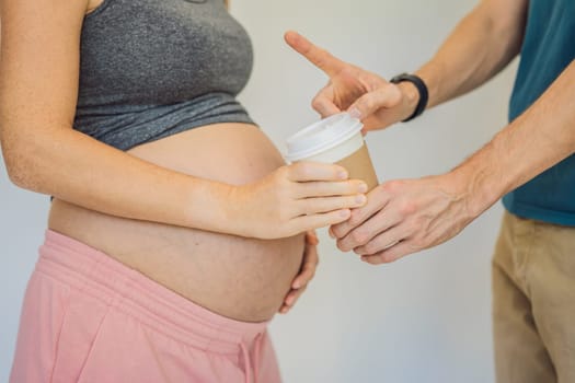 Husband forbids pregnant wife to drink coffee. A pregnant woman holds a cup of coffee in her hands. Caffeine safety, myths about coffee during pregnancy concept