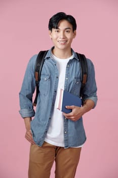Smart guy student with backpack and bunch of books smiling at camera, copy space for advertisement over pink background