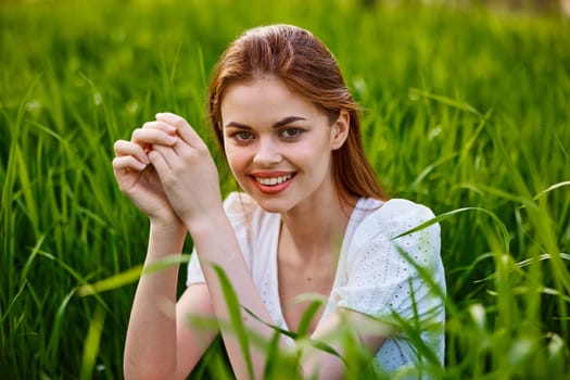 portrait of a woman sitting in the grass with her hands folded to her head
