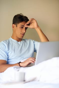 Think Ill work from home today. A handsome young men sitting in bed with his laptop.