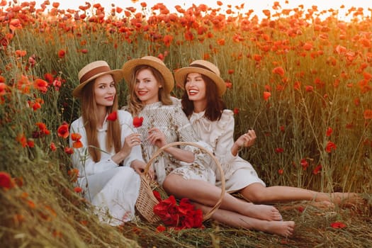 Funny girls in dresses and hats in a poppy field at sunset
