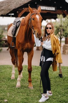 Stylish girl with glasses stands next to a horse on the street