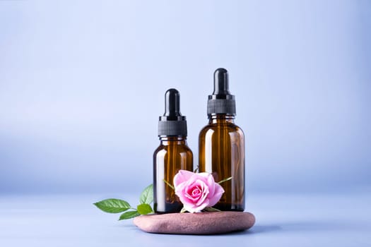 Two glass bottle with pipette for a cosmetic product with a rose on stones