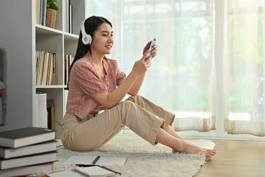Pleasant young woman using mobile phone and listening to music, podcast or audio book on wireless headphone