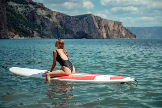Woman sap sea. Sports girl on a surfboard in the sea on a sunny summer day. In a black bathing suit, he sits on a sapa in the sea. Rest on the sea.