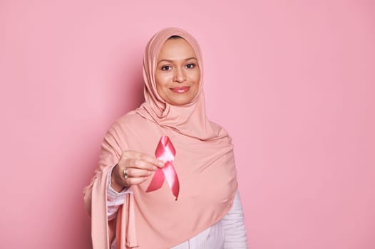 Details on pink satin awareness ribbon in Muslim Woman's hands - emblem of fighting breast cancer and supporting patients and survivors, isolated on pink background. October awareness month campaign