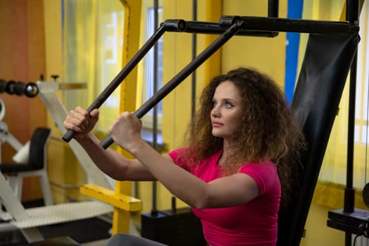 Girl with curly hair wearing pink top works out at gym